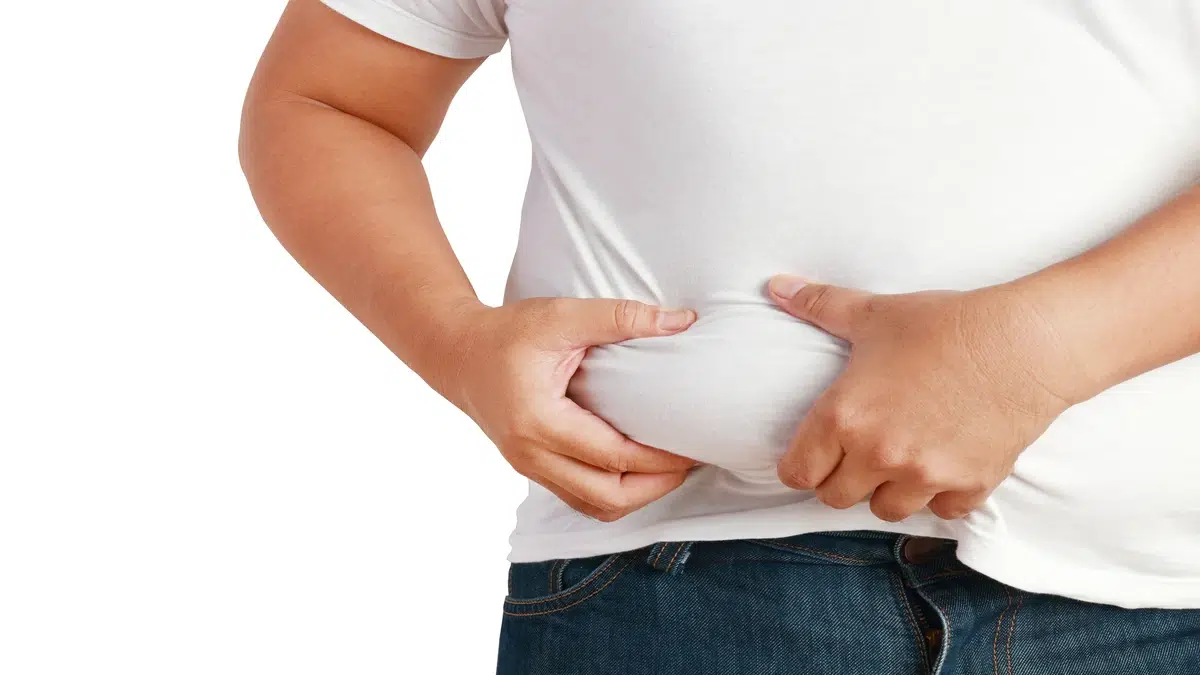 Man holding excess belly fat caused by low T, illustrating the need for testosterone deficiency treatment malaysia.